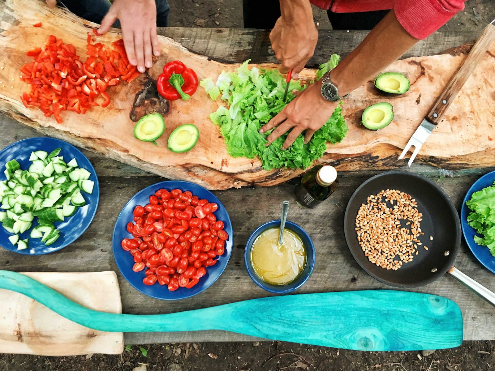 person slicing green vegetable for cooking in front of round ceramic plates with assorted sliced vegetables during daytime